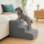 Small senior dog gently climbing up Kinstroll smoke gray gentle-slope foam stairs beside a sofa